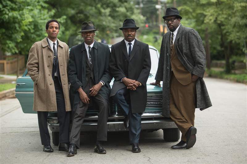 穿著大衣的金 (Oyelowo)、斯泰森 (Stetson)、戴森 (Datejust) 和其他三人在塞爾瑪 (Selma) 的一條街區(qū)街道上靠在一輛 1960 年代的汽車上。